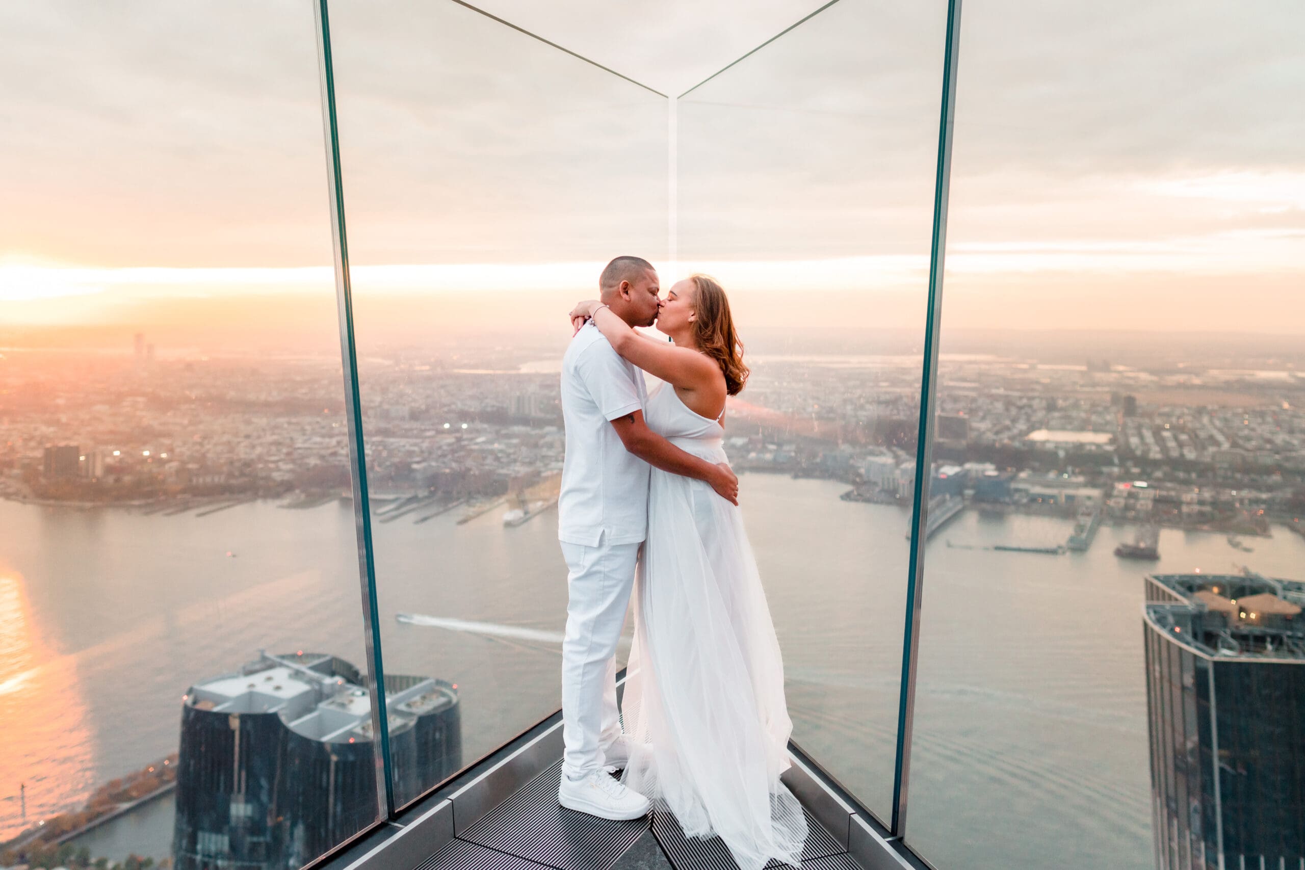 Romantic embrace at The Edge, Hudson Yards, New York: Couple shares a passionate kiss and hug, seated with water in the background, capturing the beauty of their love against the iconic skyline.