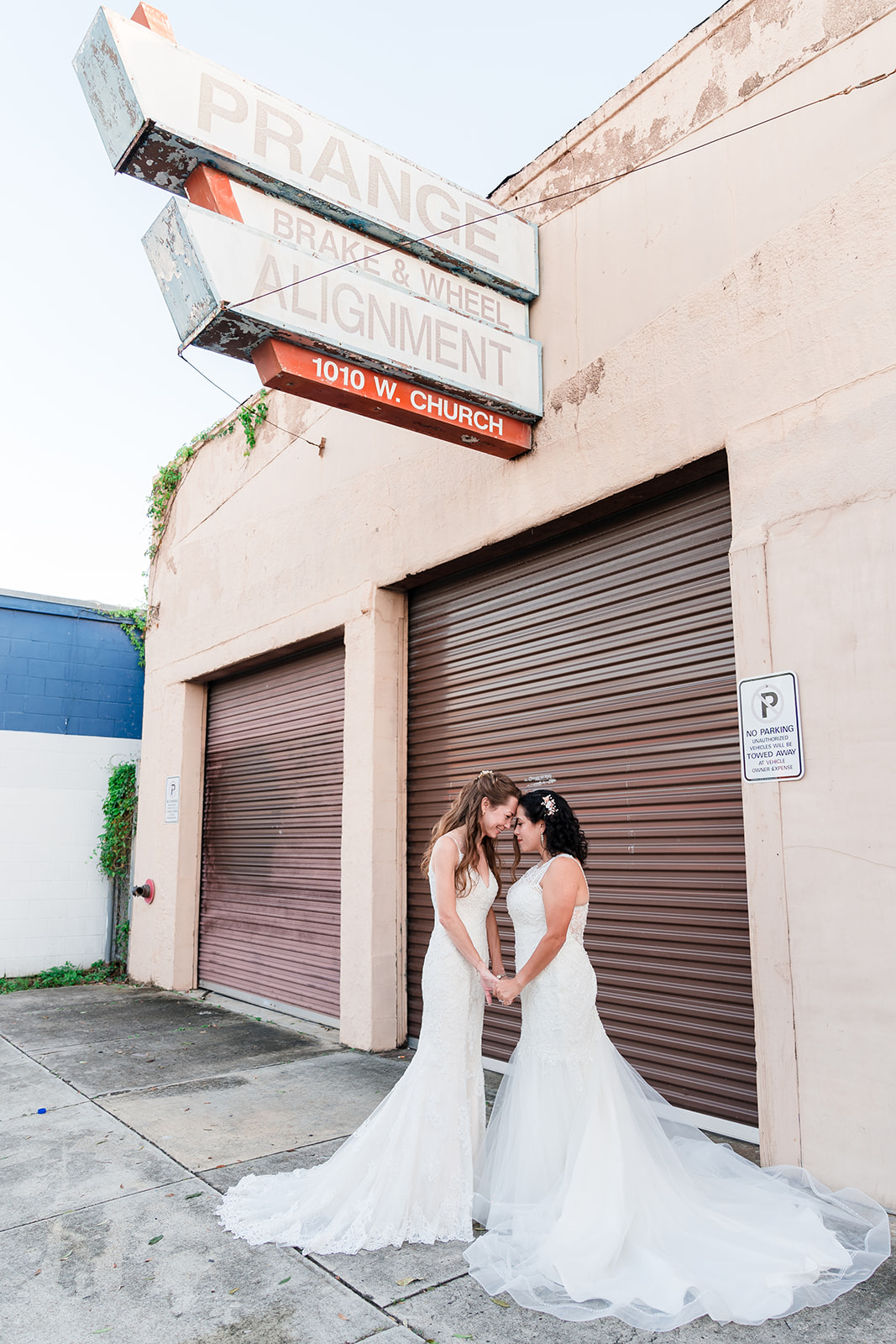 Two brides touch foreheads in front of Prange Brake and Wheel Alignment shop on Church Street in Downtown Orlando, Florida, capturing a deeply personal moment between the couple.