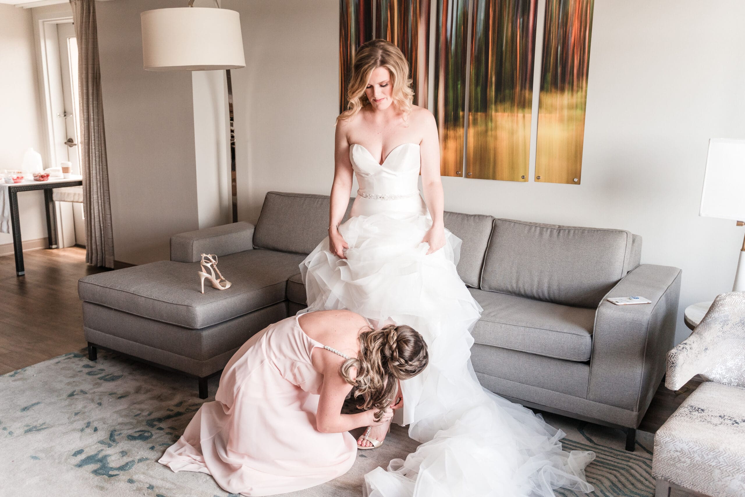 Bridesmaid helping the bride with her dress adjustments and heels as they get ready for the big day, captured in this pre-wedding photo by Jerzy Nieves Photography.