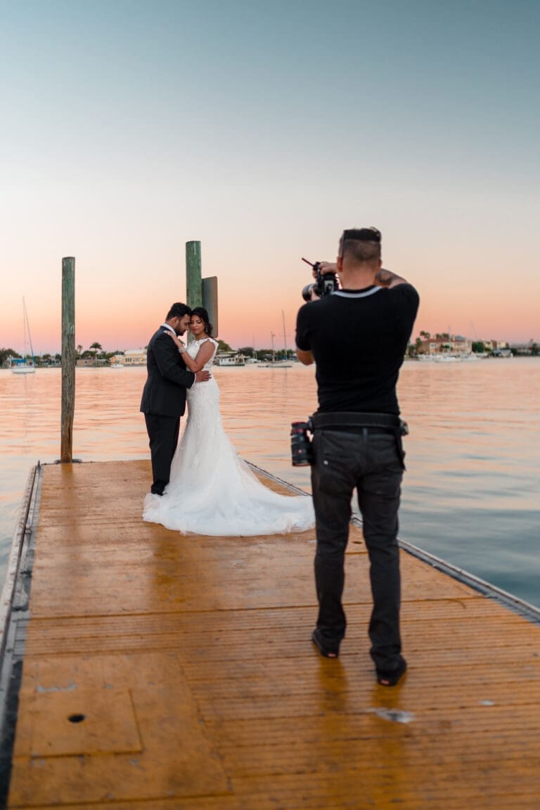 A picture of photographer Jerzy Nieves capturing a newlywed couple embracing on a dock, with water in the background.