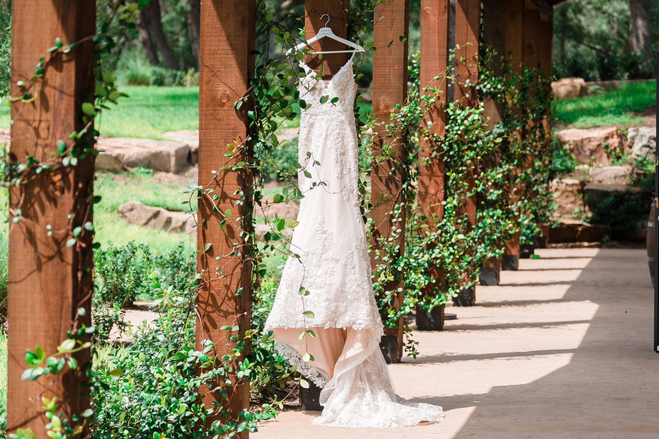 Wide shot of Bethany's wedding dress hanging on a pillar in the garden at Sterling Event Venue.