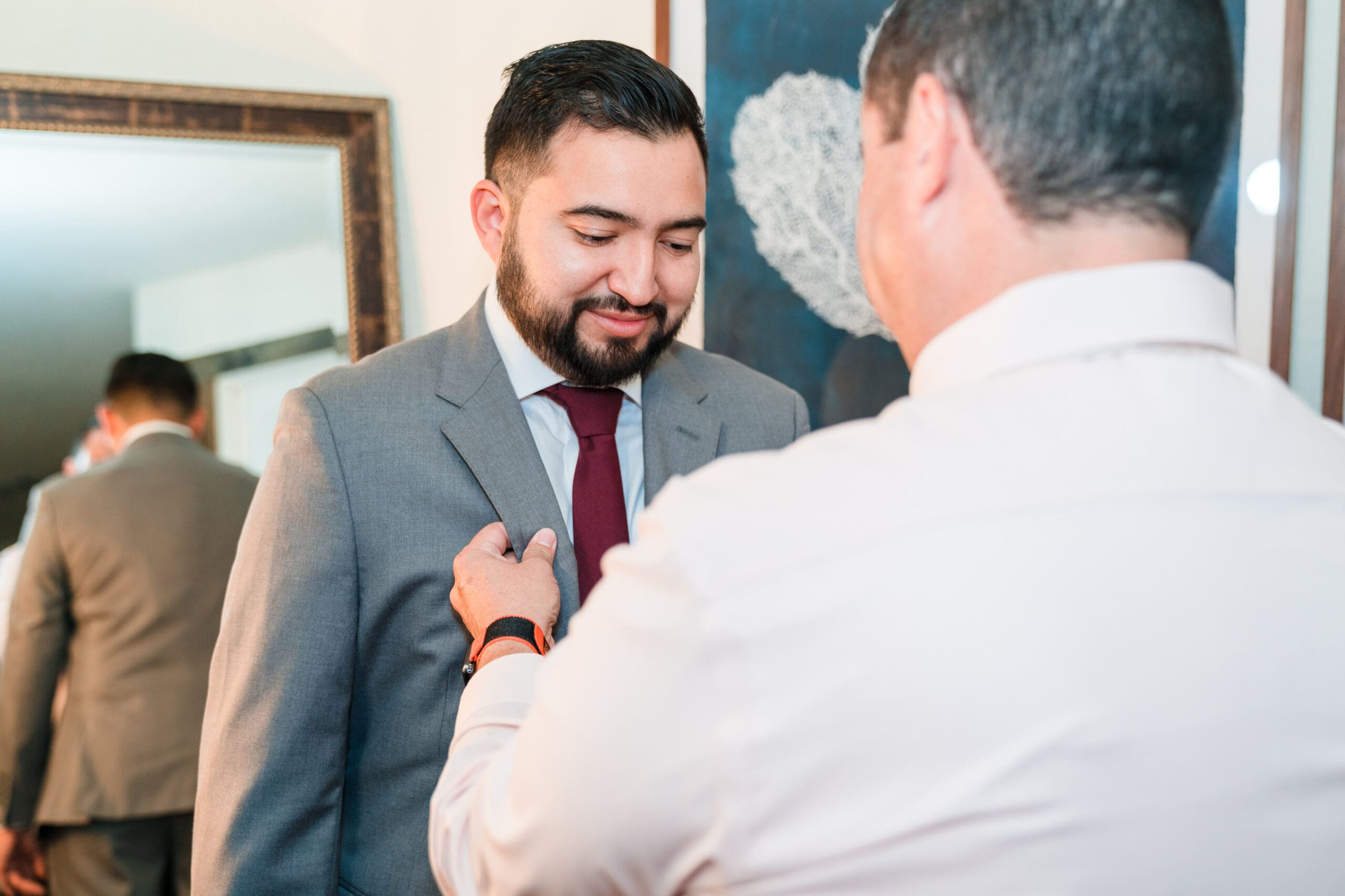 Jonah's best man fastening his sports coat in the bridal suite at Sterling Event Venue before the wedding.