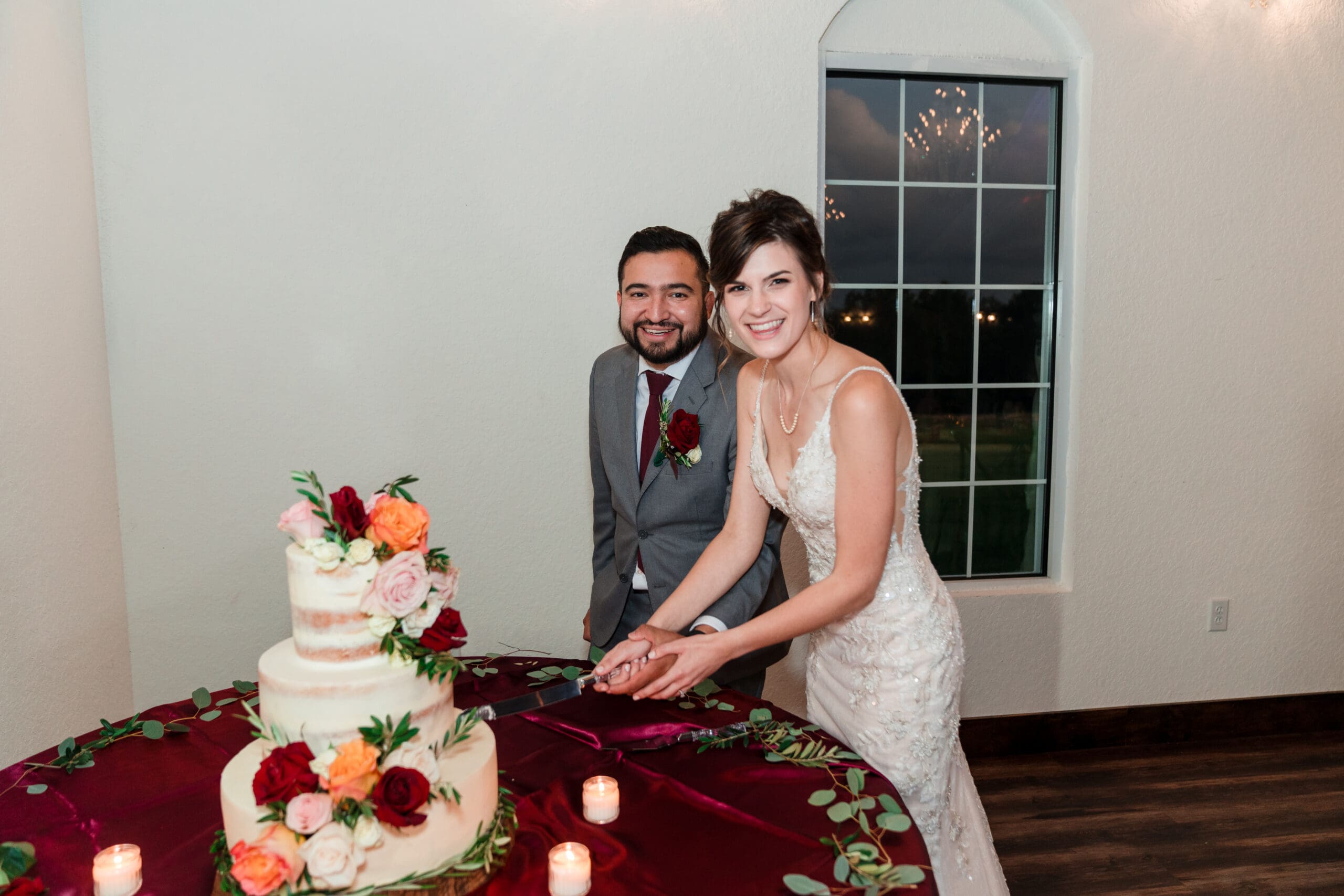 Bethany and Jonah smiling as they make the first cut in their wedding cake, surrounded by guests, during their reception at the Sterling Event Venue Reception Center.