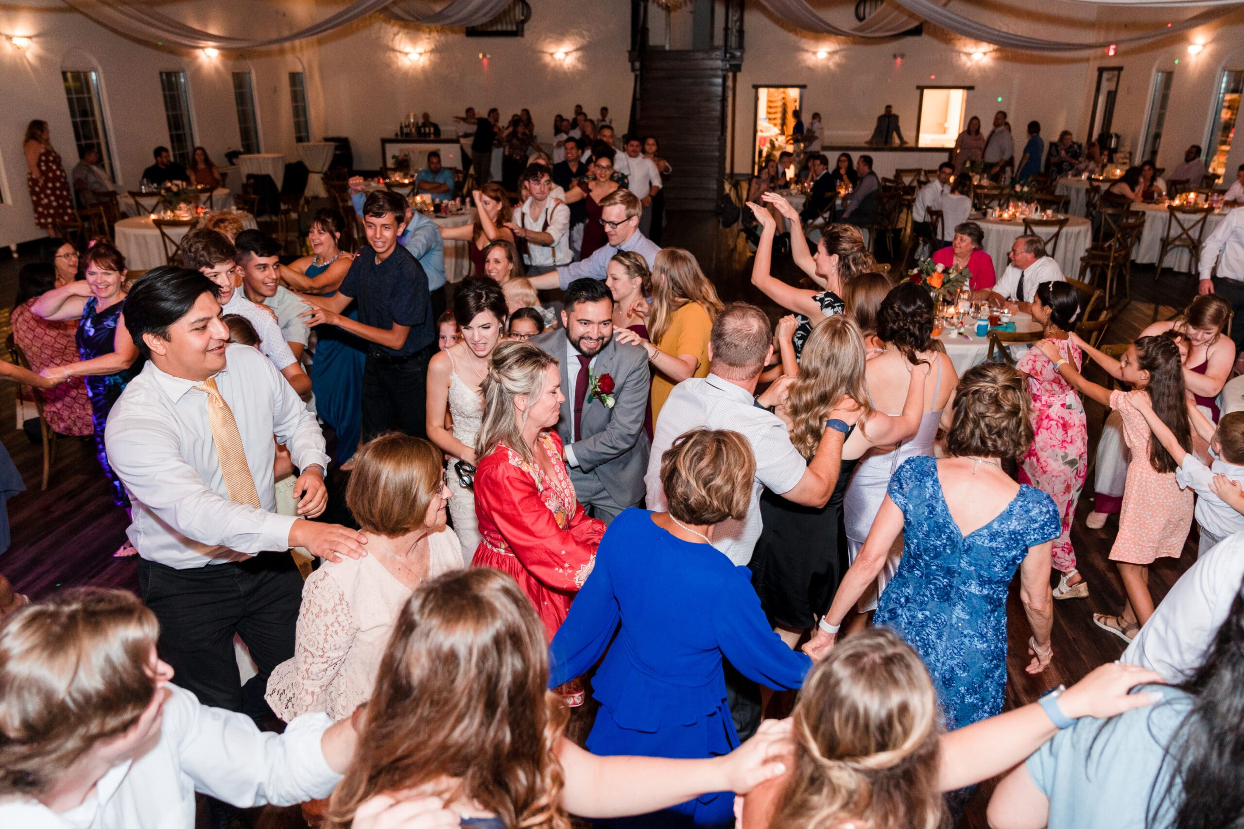 Newlyweds leading a conga line at the wedding reception, with guests joyfully dancing along, at the Sterling Event Venue Reception Center.