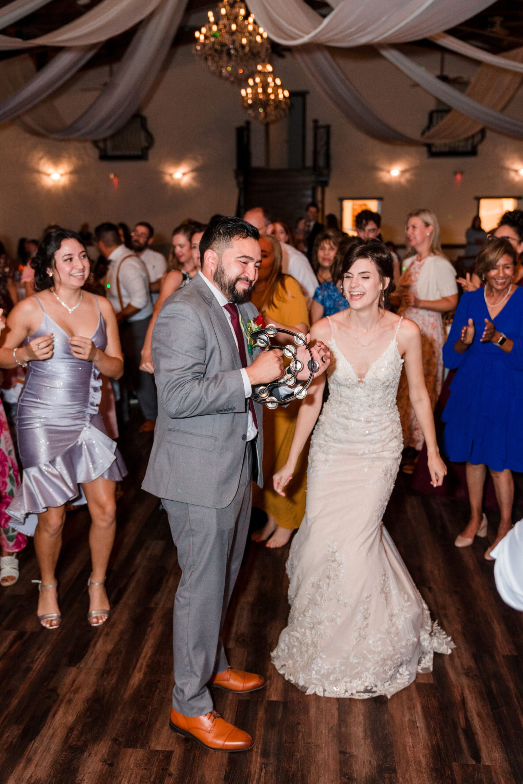 Jonah joyfully shaking a handbell on the dance floor with his new bride Bethany by his side, both immersed in the lively atmosphere of the reception at the Sterling Event Venue Reception Center.