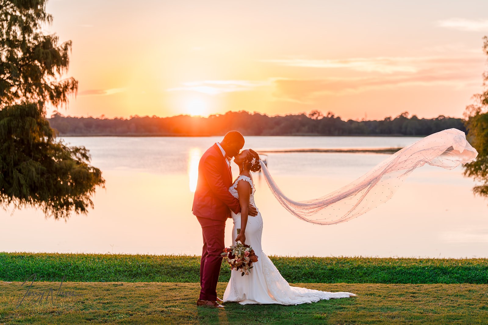 Newlyweds Shelby and Javon sharing a romantic kiss by the lake at Lake Mary Event Center, with the setting sun in the background.