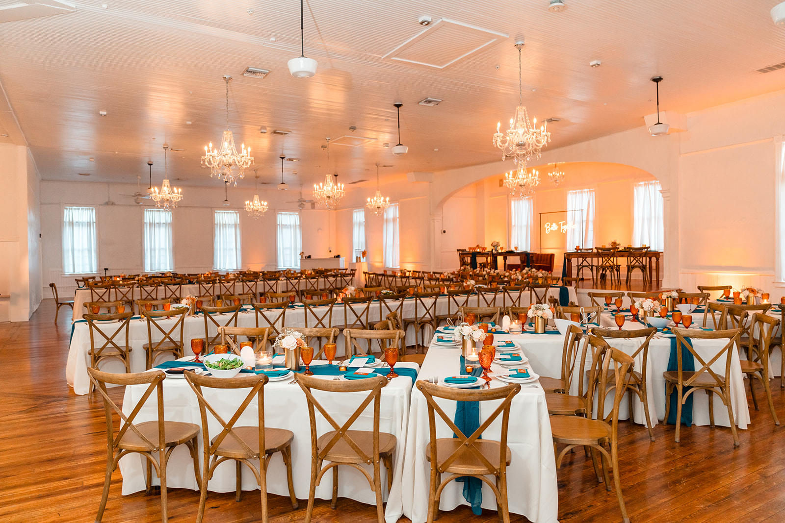 Reception hall at Venue 1902 adorned with chandeliers, decorated tables, and a stage set for the newlyweds.