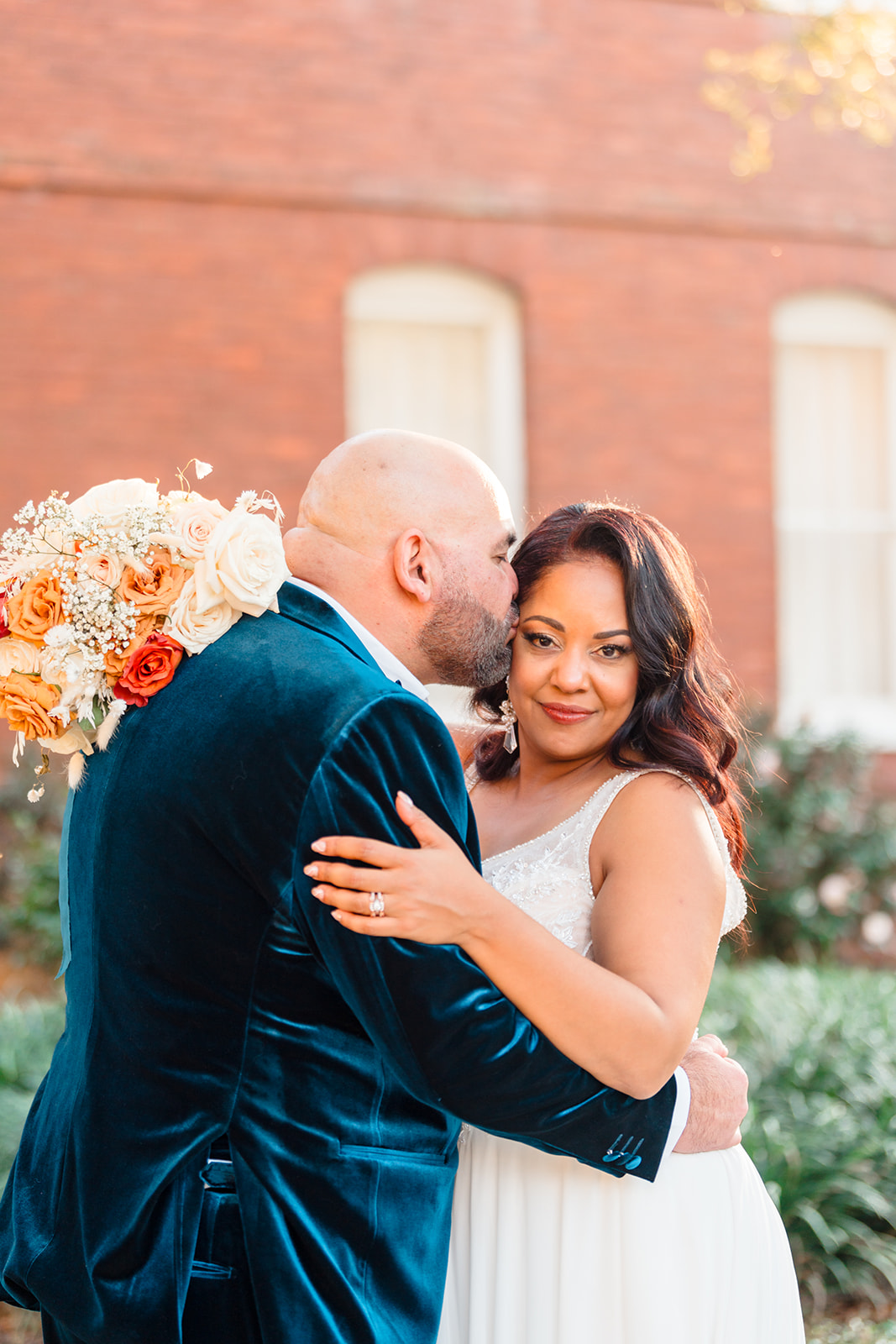 Close-up of Alberto kissing his wife's cheek as she looks at the camera outside the front of Venue 1902, captured by Jerzy Nieves Photography.