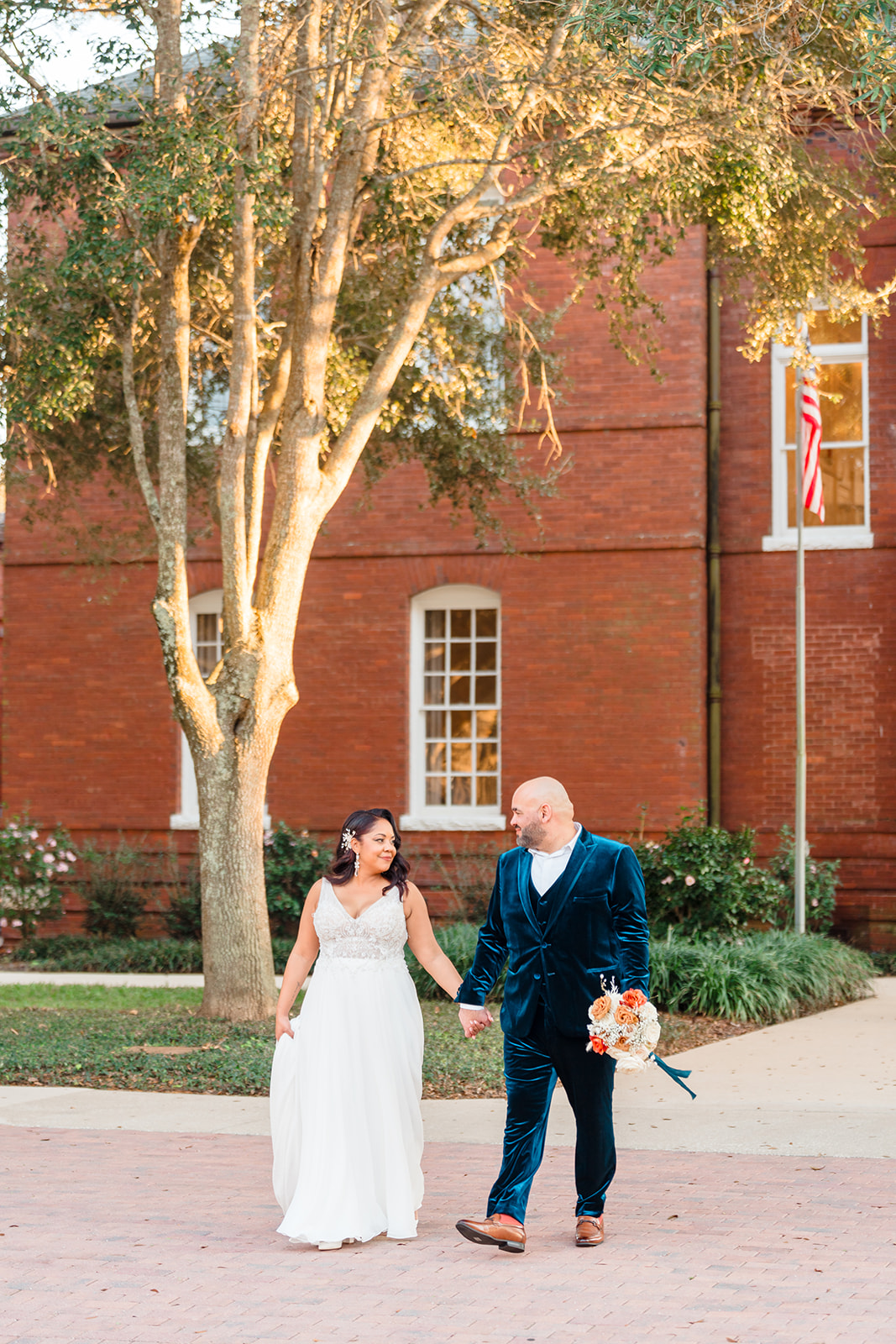 Margaux and Alberto walking together, holding hands and gazing into each other's eyes outside the front of Venue 1902, captured by Jerzy Nieves Photography.