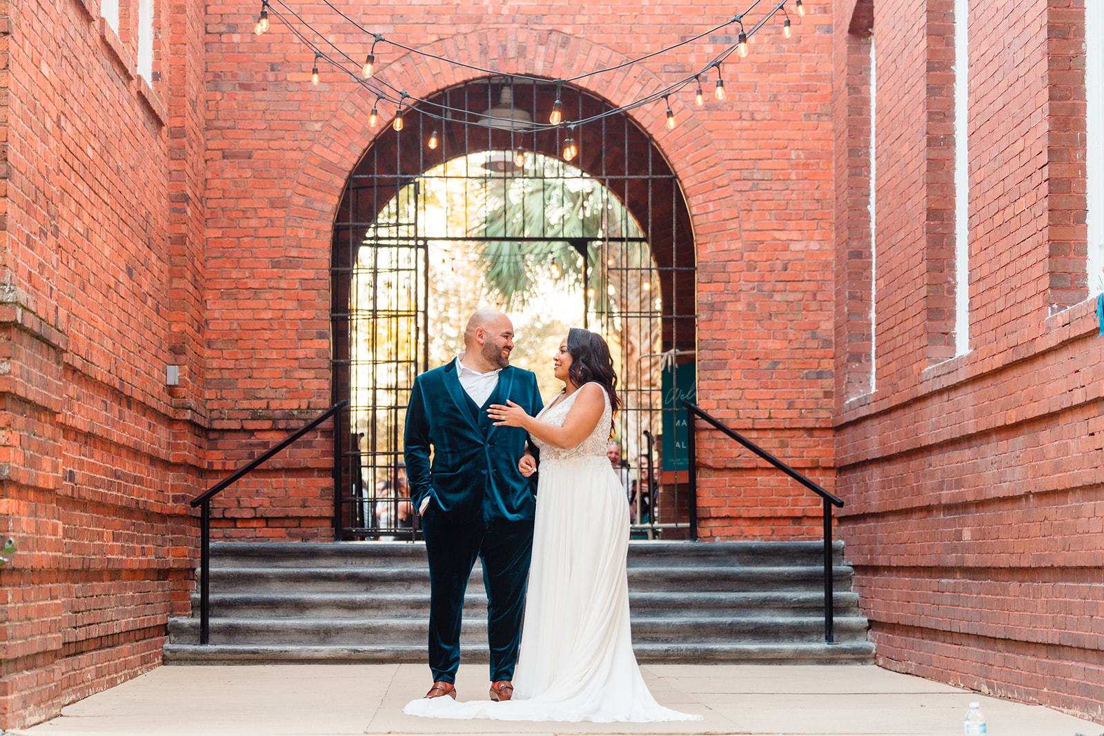 Newlyweds at the brick archway leading to the ceremony area at Venue 1902, looking into each other's eyes with love, captured by Jerzy Nieves Photography.