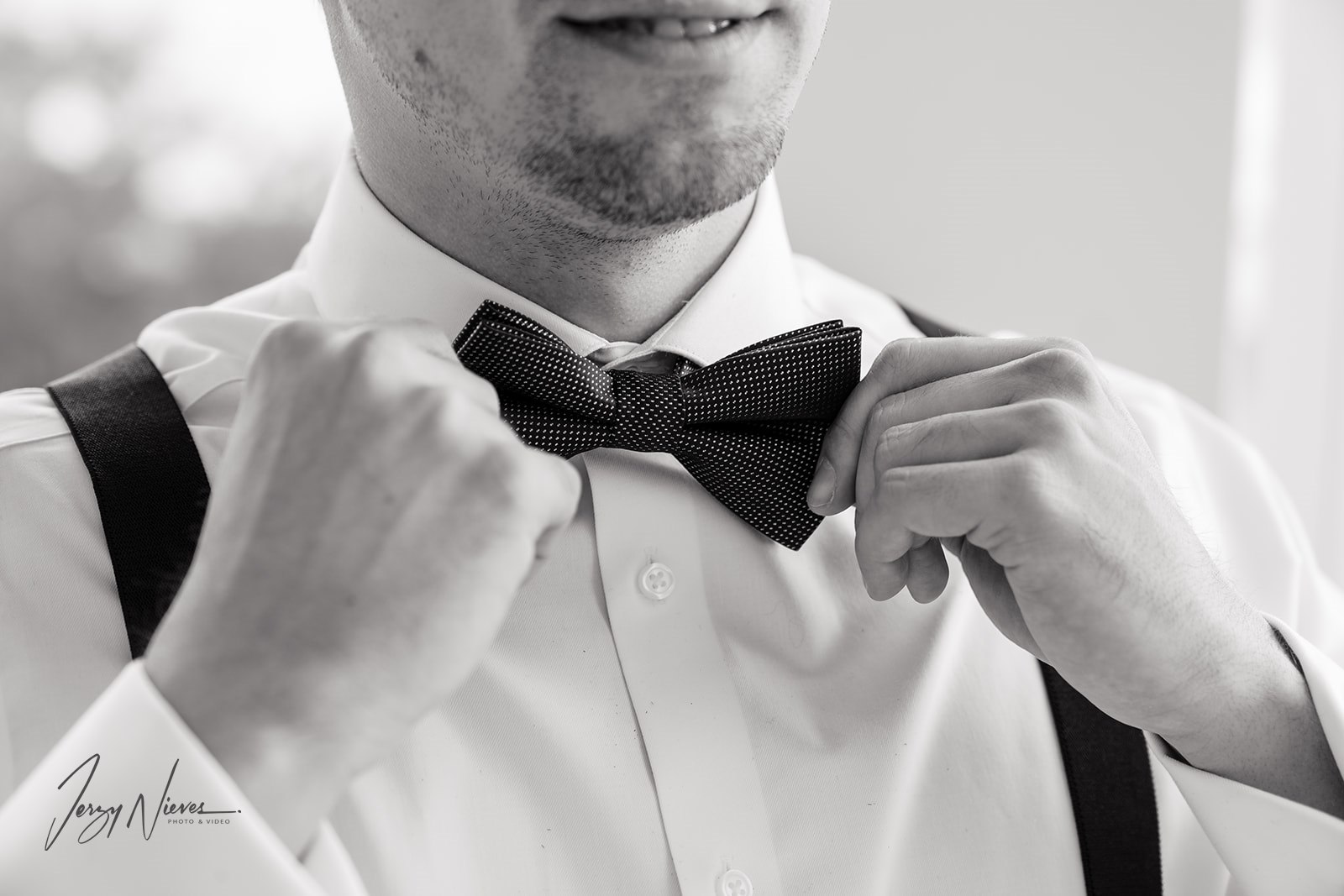 Close-up of the groom's hands adjusting his bow tie.