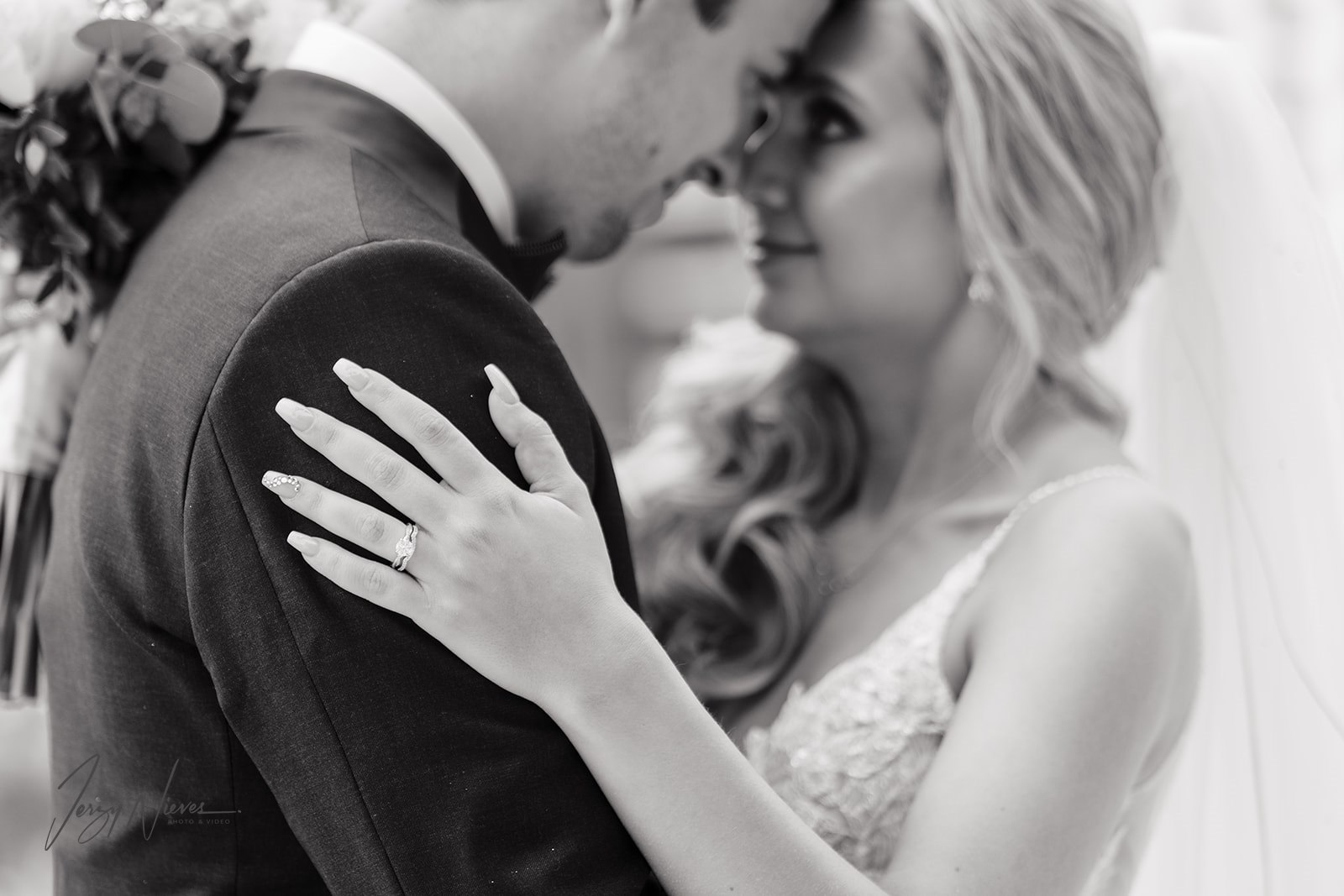 Black and white photo of the newlyweds touching foreheads while dancing, focusing on the bride's hands with her wedding bands and her hand on his shoulder.