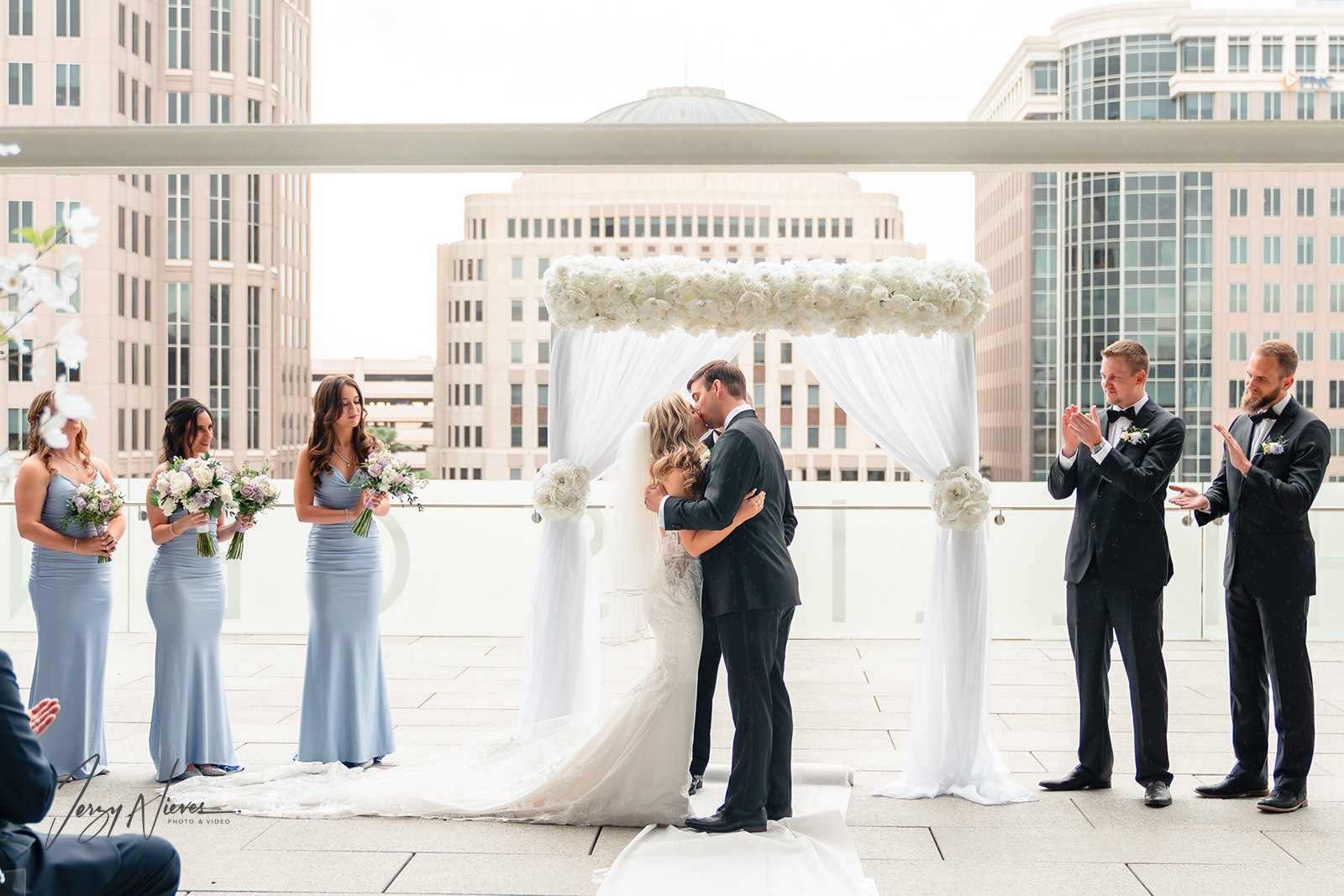 Couple kissing under wedding archway adorned with white roses and elegant white curtains at Dr. Phillips Center for Performing Arts.