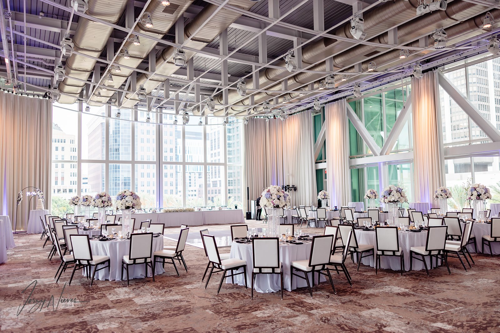 Wide shot of the reception area at the Dr. Phillips Center for Performing Arts, illuminated by natural light streaming through large windows, showcasing white tablecloths, chairs, and floral arrangements.