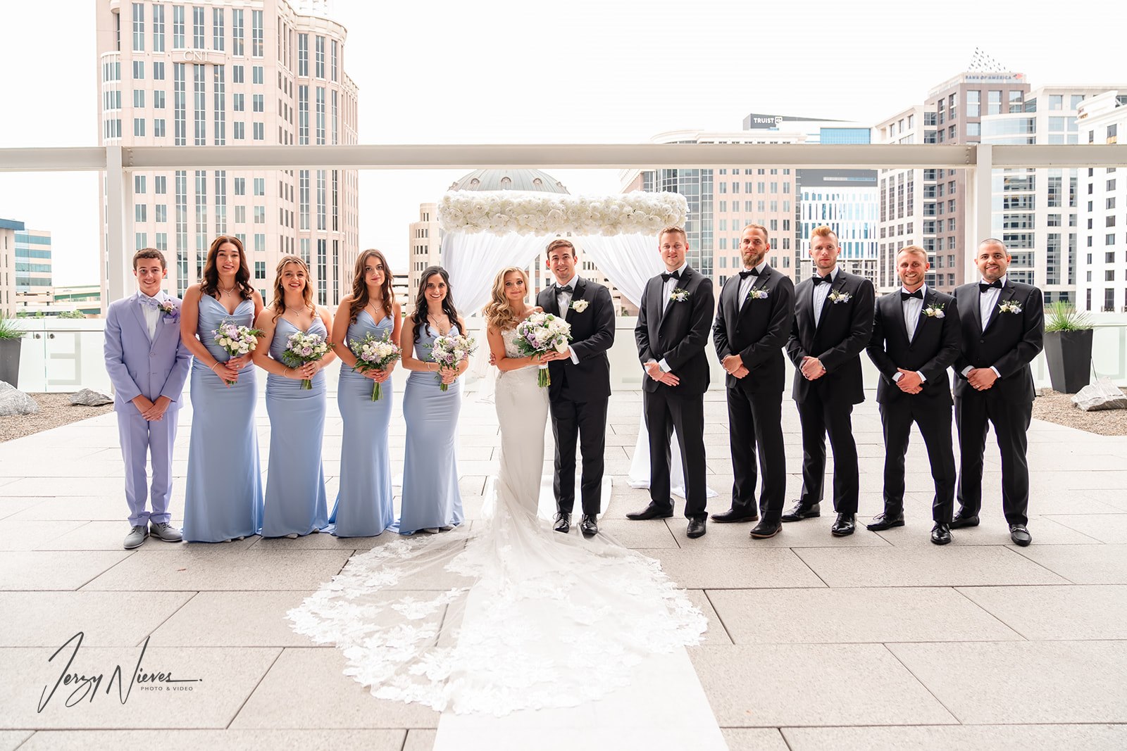 Bride, groom, and bridal party standing on the rooftop of the Dr. Phillips Center for Performing Arts, with the wedding altar and downtown Orlando skyline in the background.