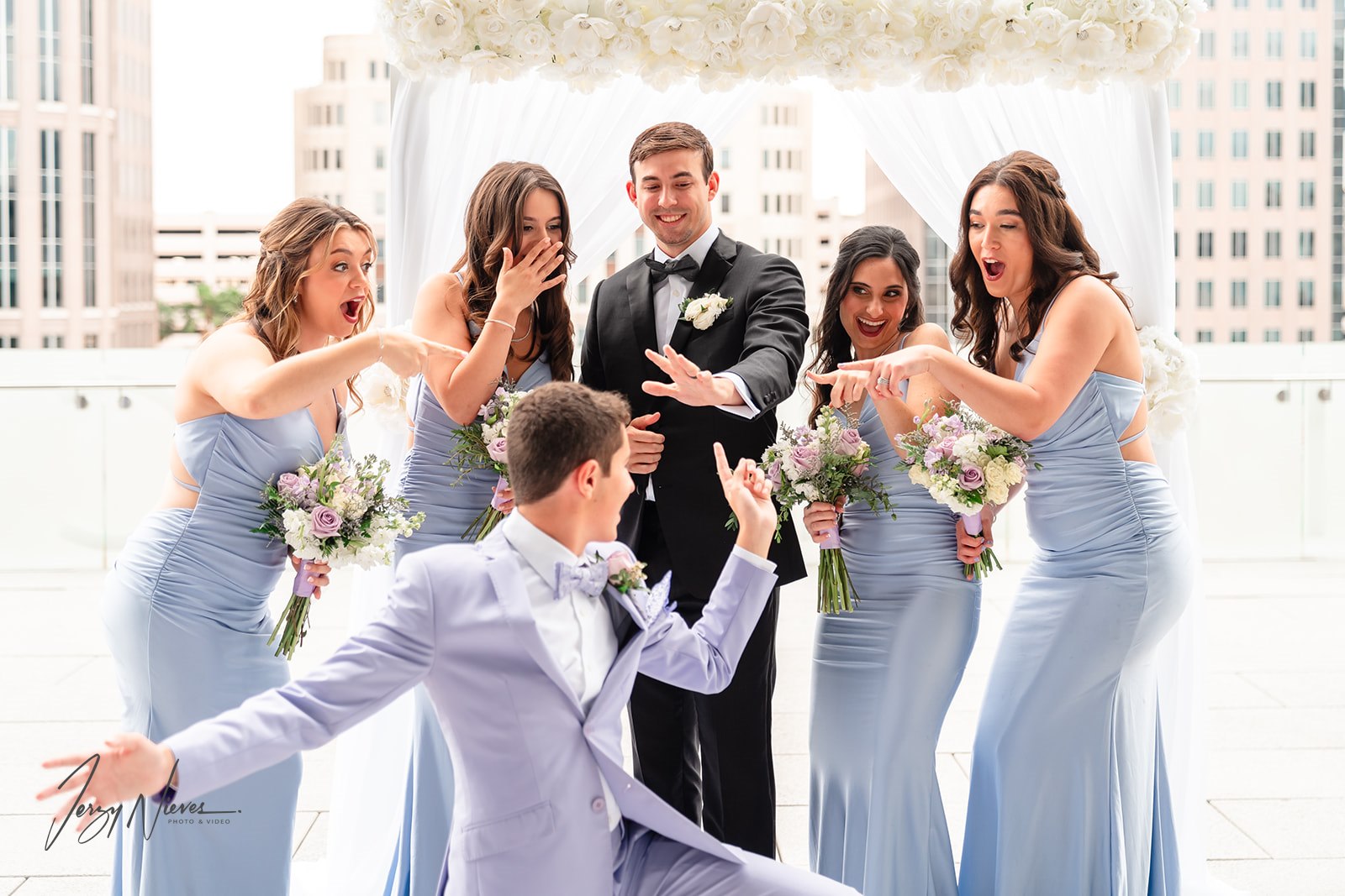 Humorous photograph of the groom at the altar, with bridesmaids pointing in surprise at his wedding ring.