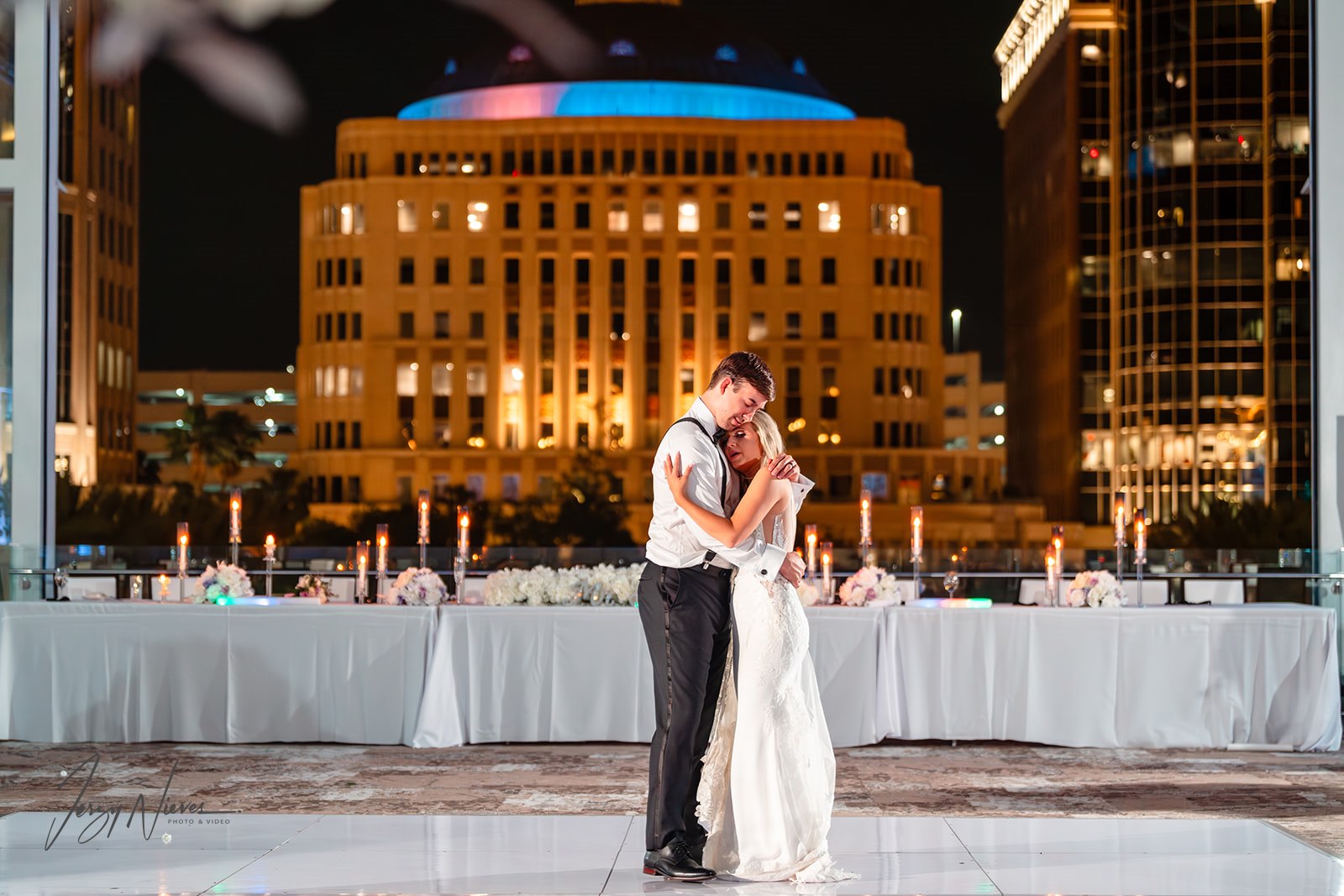 Romantic image of the bride and groom slow dancing on the rooftop of the Dr Phillips Performing Arts Center, with the night sky and cityscape in the background.