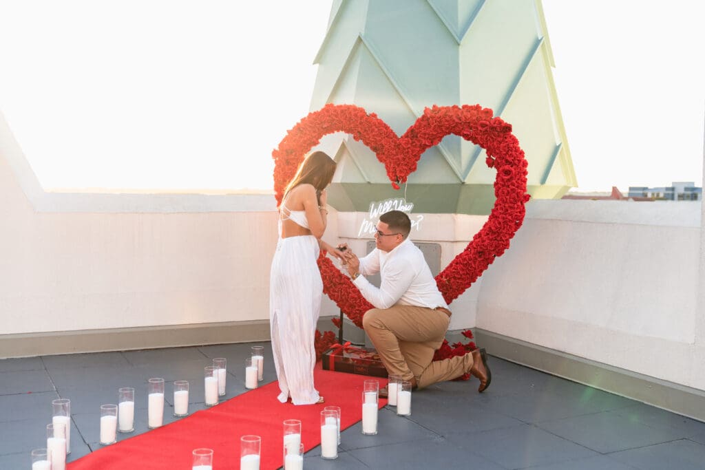 Jose placing the engagement ring on his bride-to-be's finger while on one knee, surrounded by a romantic setup.