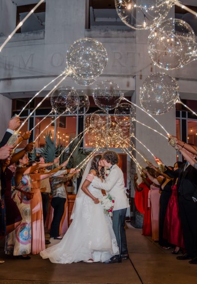 Newlyweds sharing a kiss under a canopy of glowing globe-like balloons, resembling stars