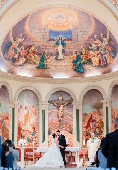 Bride and groom kiss at the altar of St. James Cathedral in Orlando, FL, with beautiful cathedral artwork in the background.